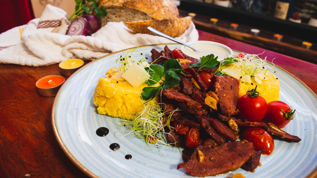 Savor a traditional Romanian meal featuring juicy beef, polenta, and fresh vegetables, perfect for a culinary adventure.